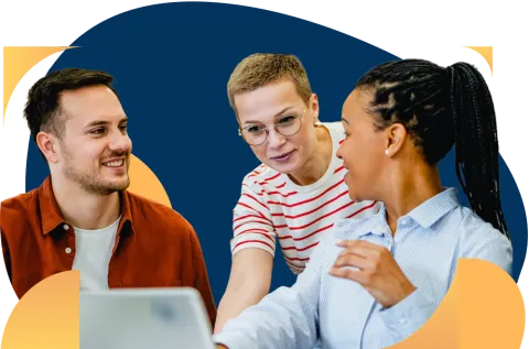 Three coworkers smile while collaborating around a laptop in an office setting